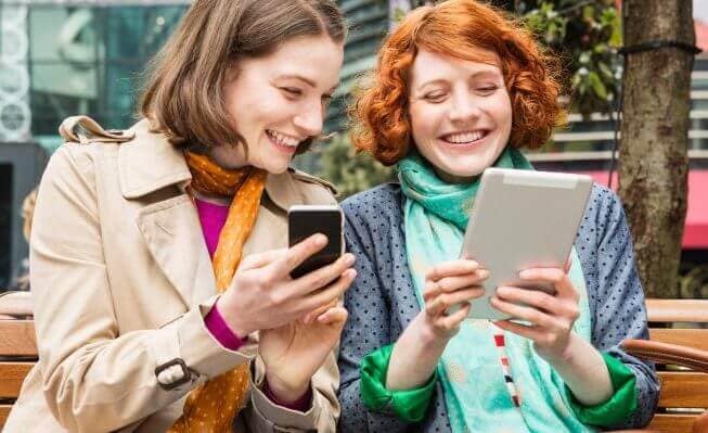 Two women exploring savings and money market accounts on their electronic devices.