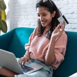 Young woman shopping online with a credit card and laptop while sitting on a sofa.