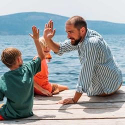 A man plays with two small children by a lake.