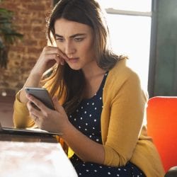 Worried woman bites her nail as she looks at her phone.