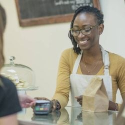 A store clerk holds a card reader as a woman pays with a contactless credit card.