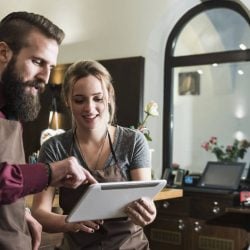 Two restaurant workers look at a digital tablet.
