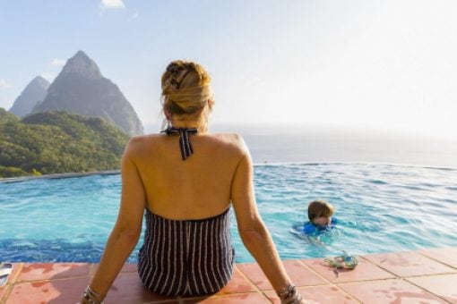 Mom sits poolside watching child swim in ocean-view pool