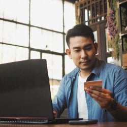 Man using laptop looks at credit card in his hand