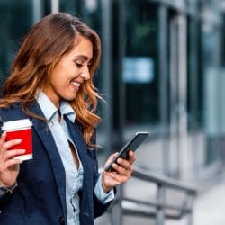 Smiling businesswoman viewing mobile phone and enjoying coffee break in front of the office.