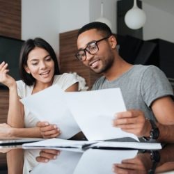 A man wearing glasses and a woman are at a desk, focused on a document in front of them.