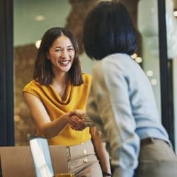 Woman in yellow shaking hands with a colleague in an office.
