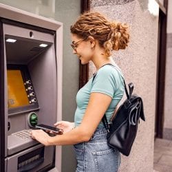 A woman stands at an ATM and holds a mobile phone.