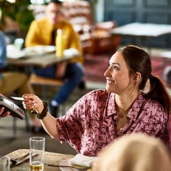 A woman using contactless payment with a credit card to pay at a restaurant.