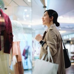 A woman in a mall admiring a dress displayed in a shop window.