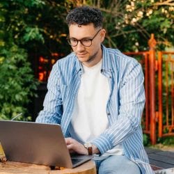 A man sitting outdoors and working on his laptop.