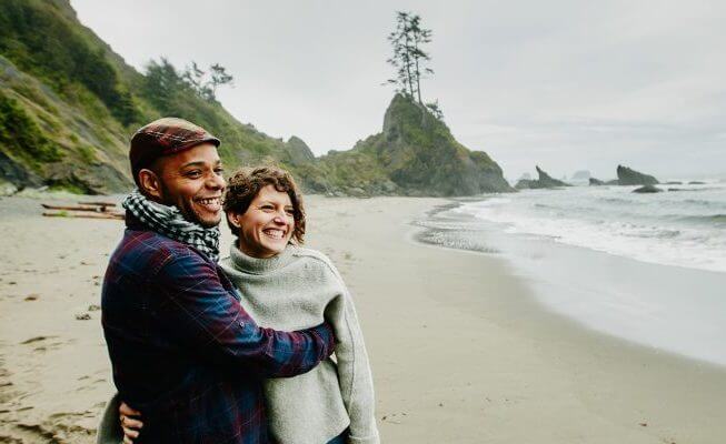 Couple walking on beach smile after talking about how they will retire early.