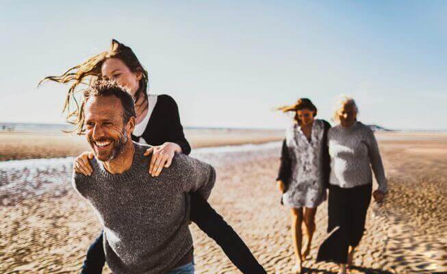 Mother and daughter discuss CD accounts while walking on a beach with their family.