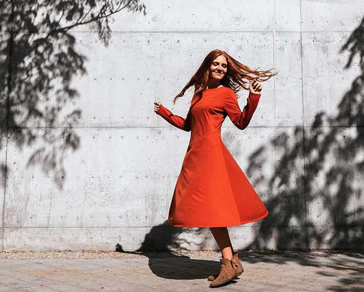 Young woman spins and smiles while walking outside after accessing her online bank account.