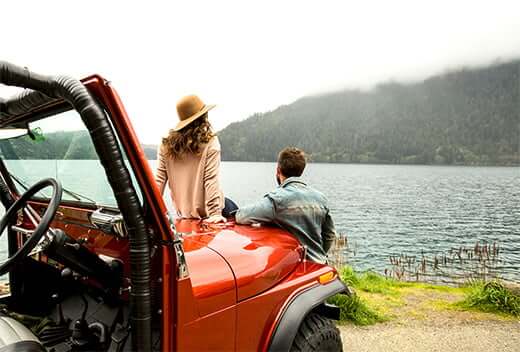 Man and woman relaxing outside of their jeep near a lake after recently opening a high yield online savings account.