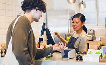 Store owner smiles while customer provides Google Pay at checkout.