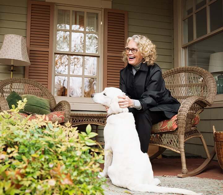 Retired woman pets dog on her front porch after transfering money into an IRA CD.