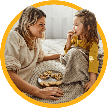 Mom and daughter sitting on bed, eating a snack.