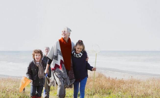 Retired woman walking on beach with grandkids.