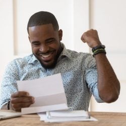 Man sitting at a desk smiles and pumps his fist as he reads his tax return.