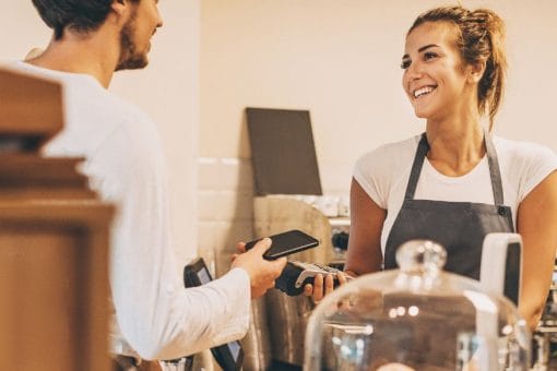 Barista holds card reader for customer to pay using digital wallet on his phone.