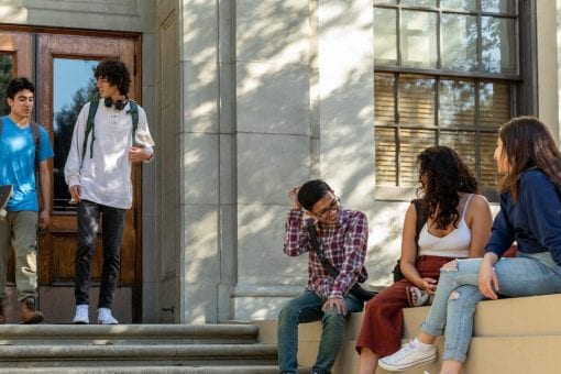 College students are standing and sitting outside of a building