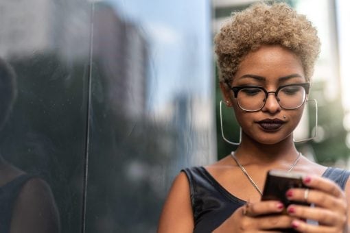 Young woman types on her mobile phone on a sunny city street