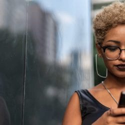 Young woman types on her mobile phone on a sunny city street.