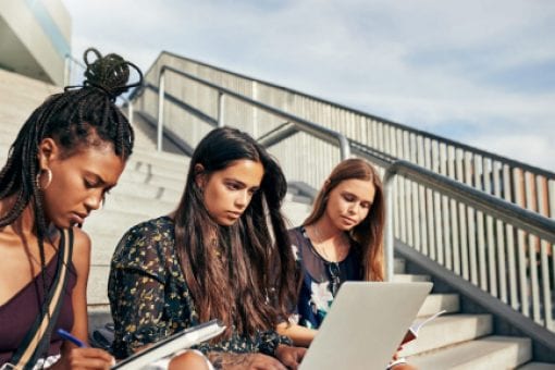 Three young women sit on concrete stairwell.