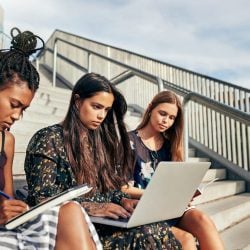 Three young women sit on concrete stairwell.