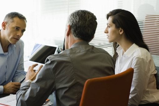 A couple sits in an office talking with another man behind his desk