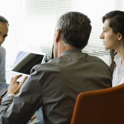 A couple sits in an office talking with another man behind his desk