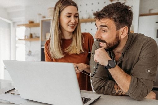 Young couple smiles together as they look at a computer screen in their kitchen