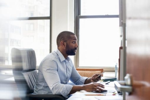 Businessman holds phone and works on computer in an office.