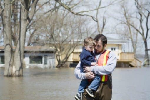 Man carries young boy through flood waters.