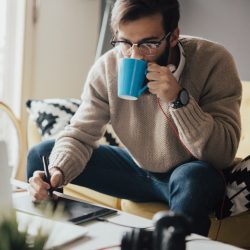 Young man sips coffee while using digital stylus on tablet