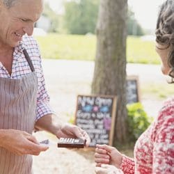 A woman hands her credit card to a shop owner holding a card terminal.