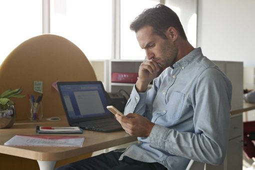 Man is concerned looking at his mobile phone at his office desk