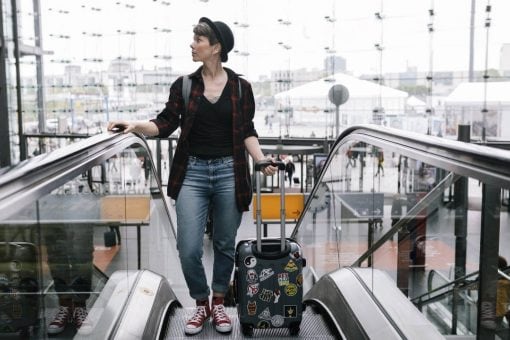 Woman rides an escalator holding a rolling traveling suitcase