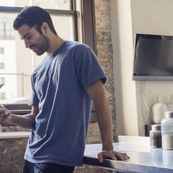 Man in his kitchen smiles looking down at his phone