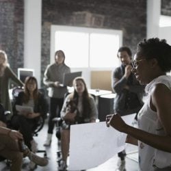 Woman holds up paper in front of a group of coworkers in an office.