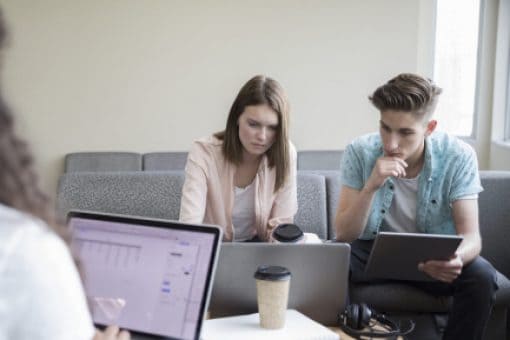 Two women and a man sit together working on laptops and a tablet.