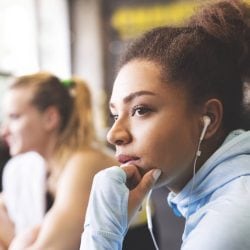 Woman in hoodie with headphones on stares off into the distance.