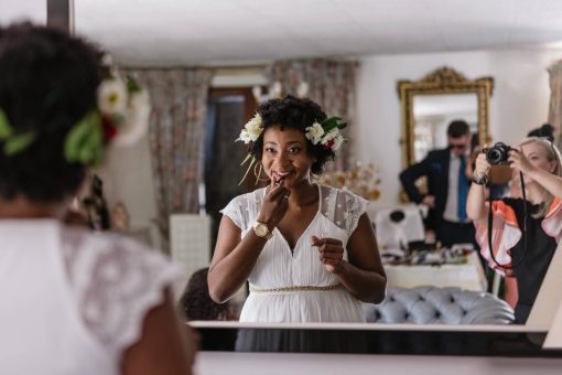 Bride-to-be puts on lipstick in mirror as photographer snaps photo behind her.