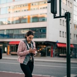 A woman looks at her mobile phone on a city street corner.