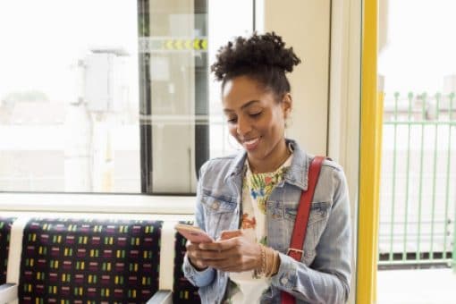 A smiling woman rides public transportation while looking at text alerts on her phone.