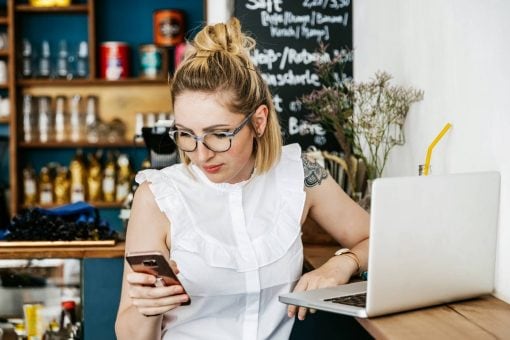 woman sitting at laptop in a café and checking her phone