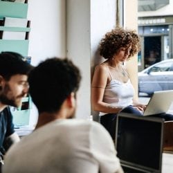 Two men and a woman using laptops in a cafe.