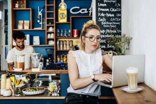 Young woman works at a laptop while sitting in a cafe