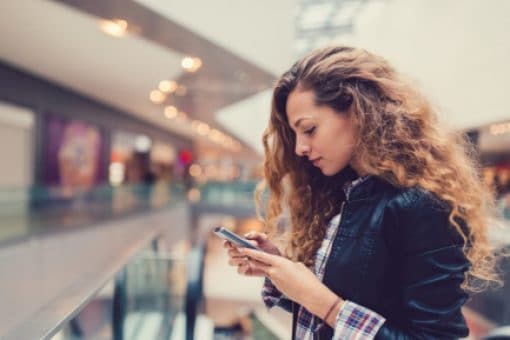 A woman standing in a mall checks her phone.